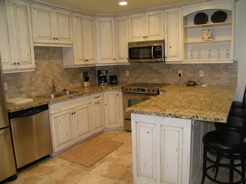 Distressed white cabinetry kitchen with granite counters and travertine tile floor