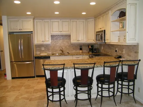 Open kitchen with white cabinets, granite counters, and wrought-iron bar stools