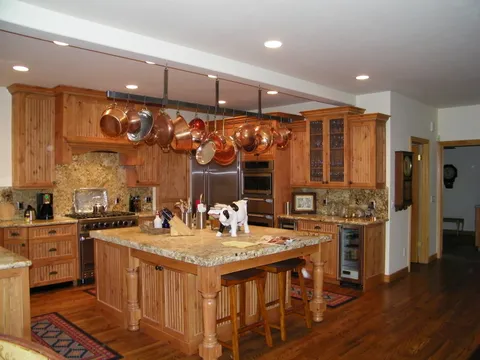 Copper pot rack, built-in ovens, and wine fridge in a pine kitchen