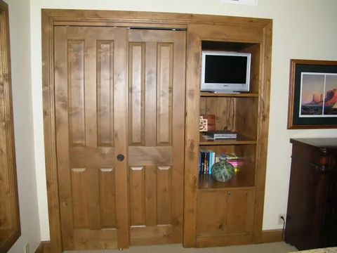 Built-in bedroom shelving with a TV niche flanking knotty-alder closet doors