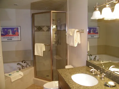 Primary bathroom with a jetted tub, corner glass shower, and granite vanity