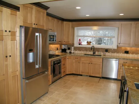 Light-wood kitchen with stainless appliances and travertine tile flooring