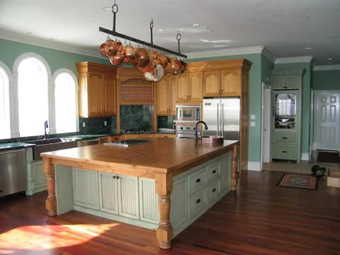 Green-walled kitchen with a copper pot rack over a butcher-block island