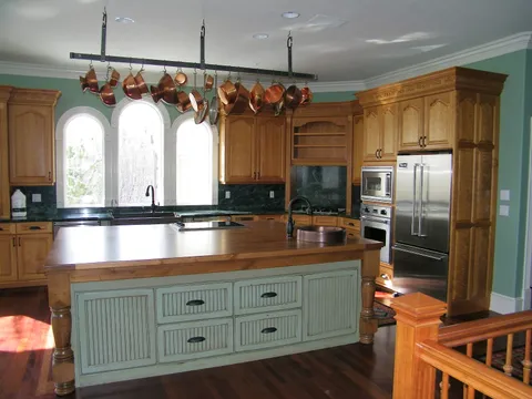 Copper pots hang above a wood-topped island in a sage-green kitchen