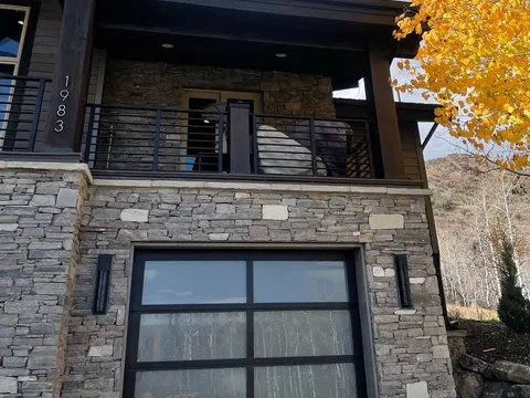 Dark-sided home exterior with a stone chimney, garage door, and autumn tree