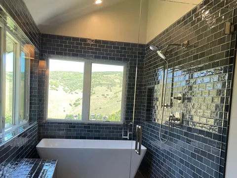 Freestanding tub in a dark-tiled bathroom with large windows