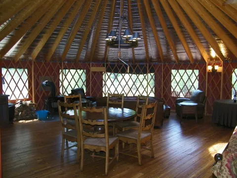Yurt kitchenette with a wood stove, dining table, and leather sofas