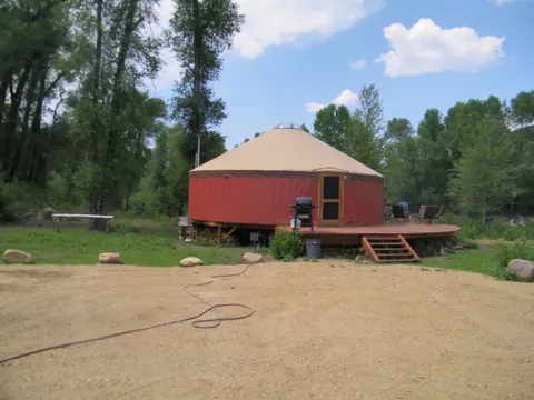 Round yurt with a tan roof and red canvas on a wood deck