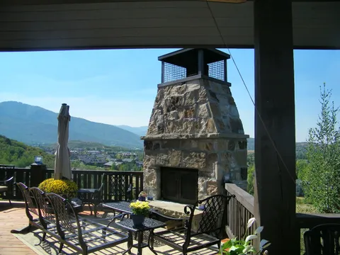 Stone outdoor fireplace with a mesh chimney cap and mountain backdrop