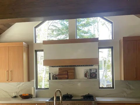 Kitchen sink beneath a window with wood cabinets and hanging cookware