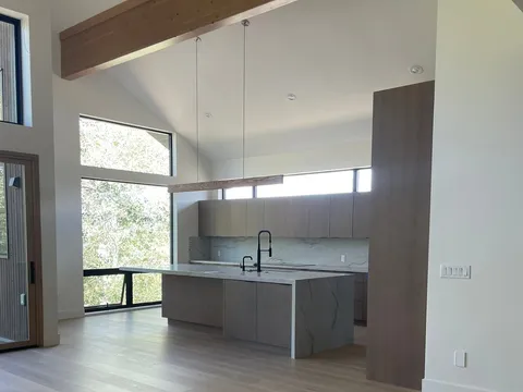 Open room with wide plank floors, windows, and a kitchen at the far end