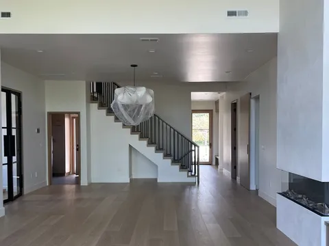 Open hallway with staircase, light wood floors, and stone fireplace edge