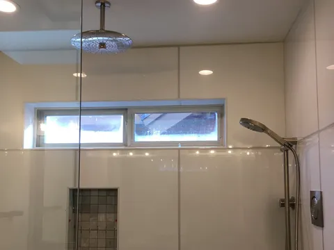 Glass shower enclosure with white tile and a high window