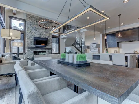 Dining table under a modern linear light fixture near an open kitchen