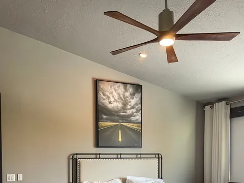 Bedroom with upholstered bed, ceiling fan, and framed artwork