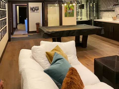 Lower-level lounge with pale sofas, stone walls, and a wood-plank ceiling