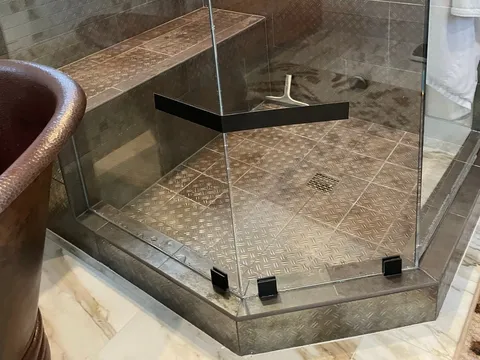 Glass-enclosed shower with stone tile and a built-in bench
