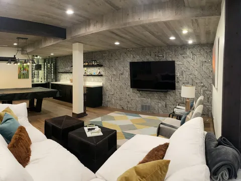 Wide view of a basement lounge and bar with pale sofas and a wood ceiling
