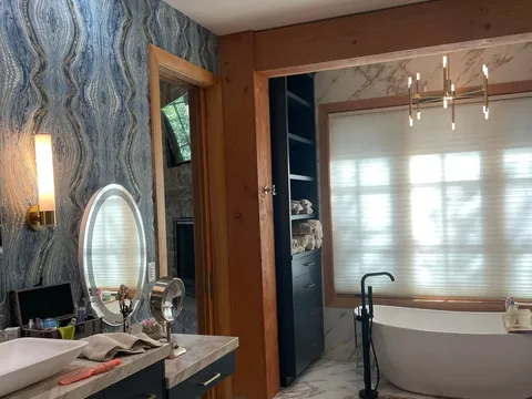 Bathroom with freestanding tub, dark vanity, and patterned wallpaper